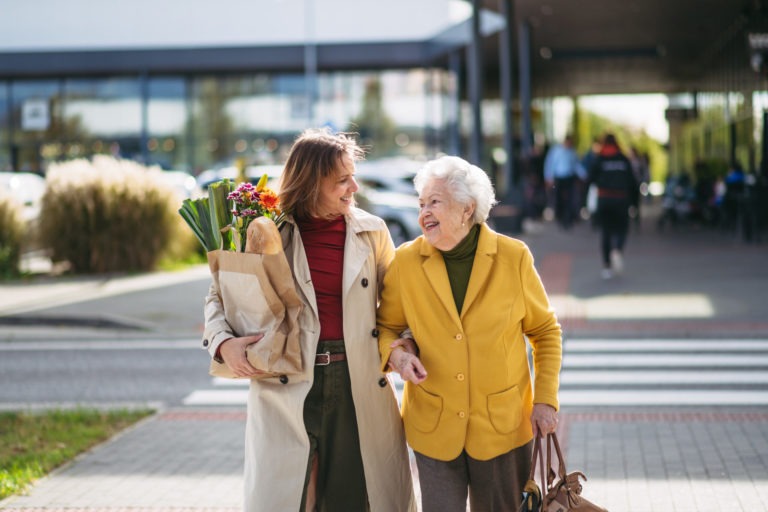 mature granddaughter carrying groceries out to her grandmother's car. senior woman shopping at the shopping centre, needing help loading groceries into car.